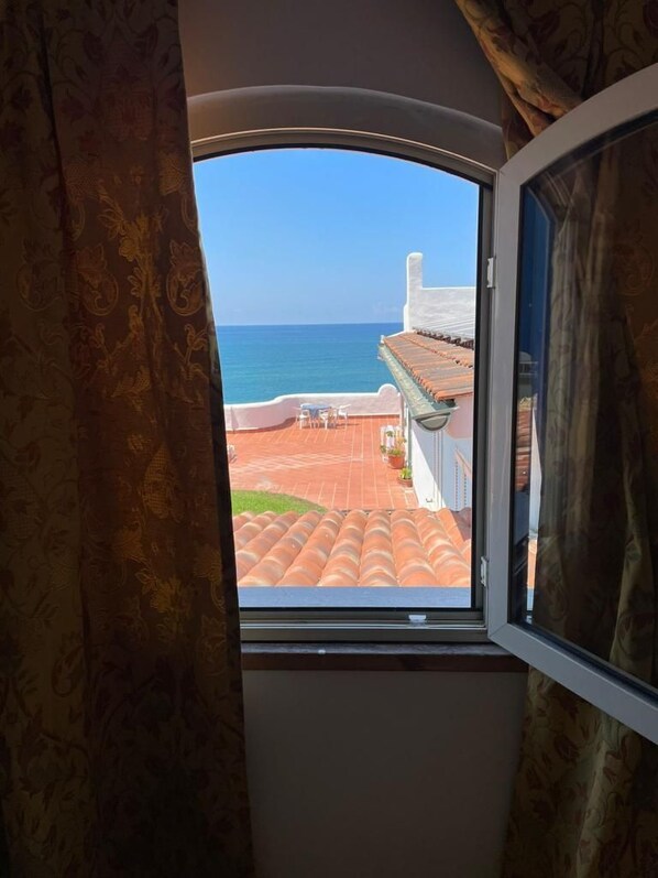 Ein Fenster mit Blick auf eine Küstenlandschaft, darunter ein Gebäude mit rotem Ziegeldach und einem strahlend blauen Himmel.