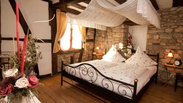 A bedroom with a stone wall, a bed with white bedding, and a canopy. - Rosenhäuschen Nostalgie 4-star vacation home (Kirnsulzbach)