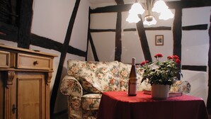 A cozy room with a floral sofa, a wooden cabinet, a table with a red tablecloth, and a potted plant with red flowers. - Rosenhäuschen Nostalgie 4-star vacation home (Kirnsulzbach)