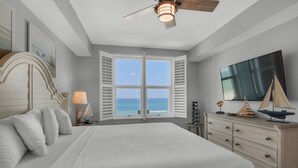 A bedroom with a large bed, a dresser, a ceiling fan, and a window with a view of the ocean. - 302 -Luxury Gulf-Front Condo | 3 Bedrooms | Sleeps 8+ Free Beach Chairs! (Panama City Beach)