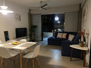 A modern living room with a sofa, dining table, chairs, a TV, and a ceiling fan.