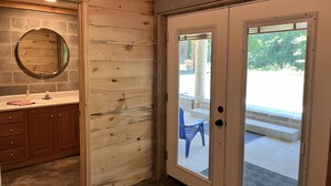 A wooden interior with a bathroom, a door leading outside, and a view of the outdoors.