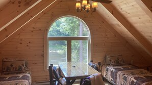 A cozy cabin with a wooden interior, a large arched window, a dining table, and two patterned sofas.