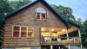 A log cabin with a covered porch, multiple windows, and a staircase leading to an upper level.