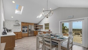 A modern kitchen with wooden cabinets, a central island, and a dining area with a view to the outdoors. - Beach Access, Walk to village, Sunsets included (Sarasota)