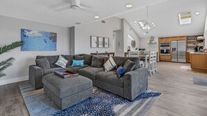 A modern living room with a grey sectional sofa, a small ottoman, and a blue patterned rug. A ceiling fan is visible, and the room has a large window. - Beach Access, Walk to village, Sunsets included (Sarasota)