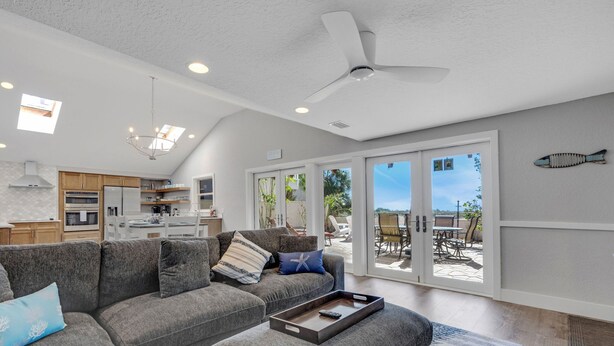 A modern living room with a grey sectional sofa, a coffee table, and a ceiling fan. There is a sliding glass door leading to an outdoor patio area. - Beach Access, Walk to village, Sunsets included (Sarasota)