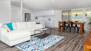 Ein modernes Wohnzimmer mit einem weißen Sofa, einem Couchtisch und einem Essbereich mit einem Holztisch und Stühlen.