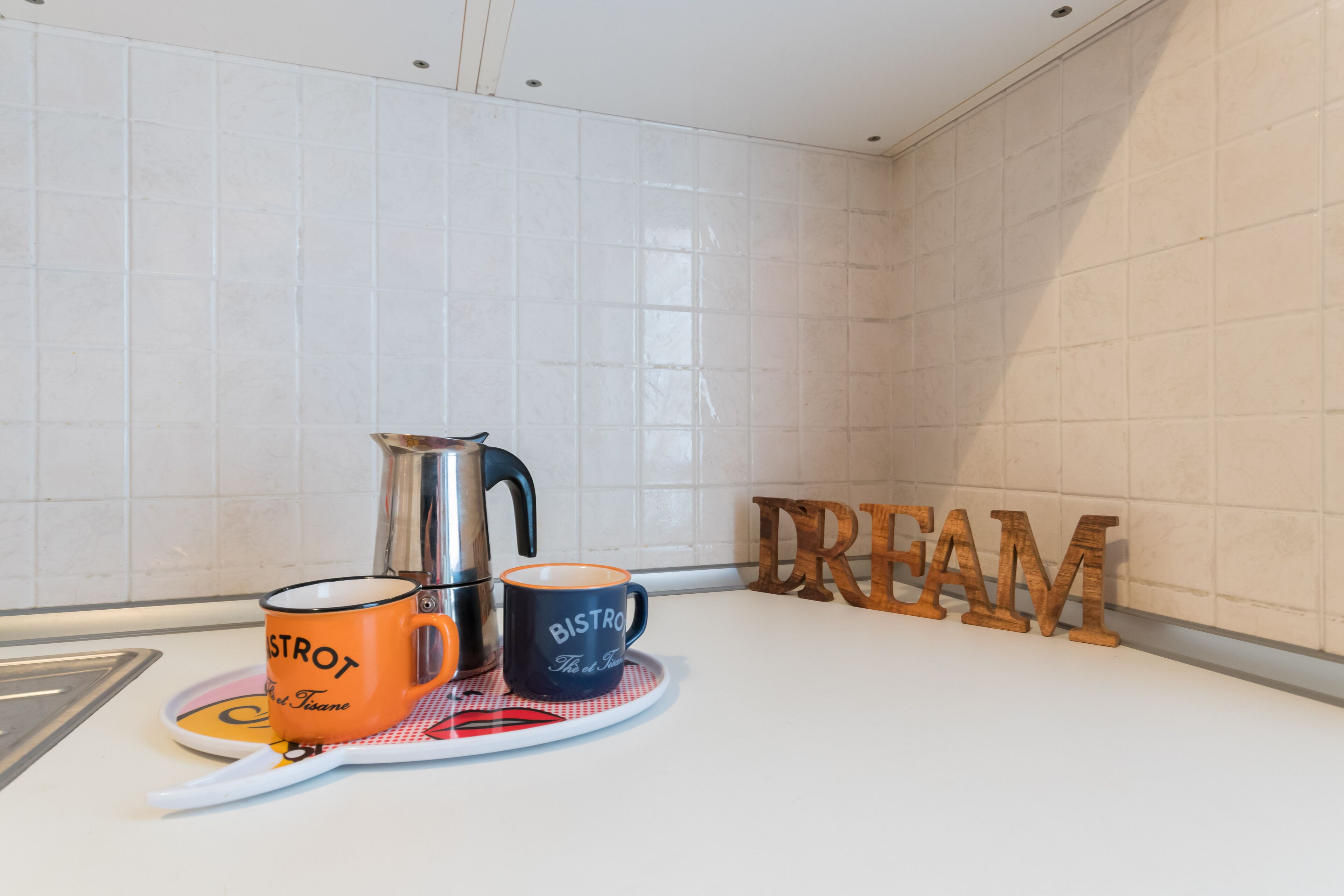 Un piano di lavoro della cucina con una moka, due tazze, un piatto e un cartello di legno con la scritta "CREAM".