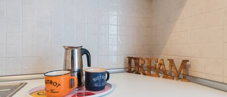 A kitchen counter with a coffee maker, two mugs, a plate, and a wooden sign that reads "CREAM".