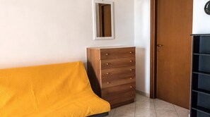 A room with a wooden dresser, a yellow sofa, a door, and a mirror on the wall.