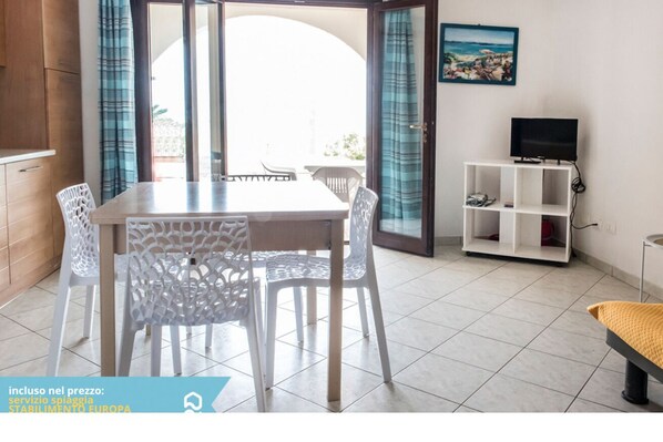A room with a dining table, chairs, a TV, and a view through a glass door.