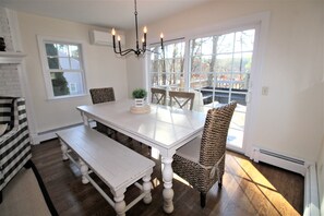 A dining area with a white table, bench, wicker chairs, and a chandelier. - Pristine Pond-Side Escape Adjacent to Dennis Pines Golf Course (2208) (South Dennis)
