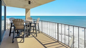 A balcony with a table and chairs overlooking a beach.