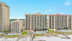 A high-rise hotel with multiple balconies, a swimming pool, and a beach area.