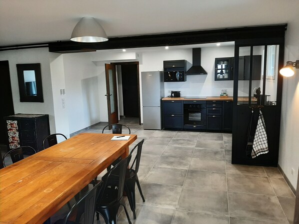 A modern kitchen with dark cabinetry, a wooden dining table, and a tiled floor. - Very large room with an industrial vibe (Châtel-Guyon)