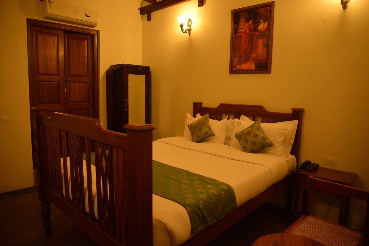 A bedroom with a wooden bed, a nightstand, a bedside table, a mirror, and a wall-mounted light fixture.