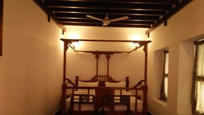 Un lit traditionnel à baldaquin, doté d’une tête de lit et d’un pied de lit en bois, flanqué de deux chaises en bois avec des coussins.