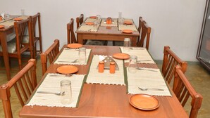 Un coin repas avec des tables et des chaises en bois, agrémenté d’assiettes et de couverts orange, et un tableau encadré accroché au mur.