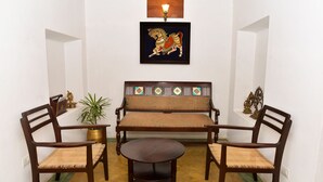 Une pièce comprenant un canapé, deux chaises en bois, une petite table ronde et un tableau encadré accroché au mur.