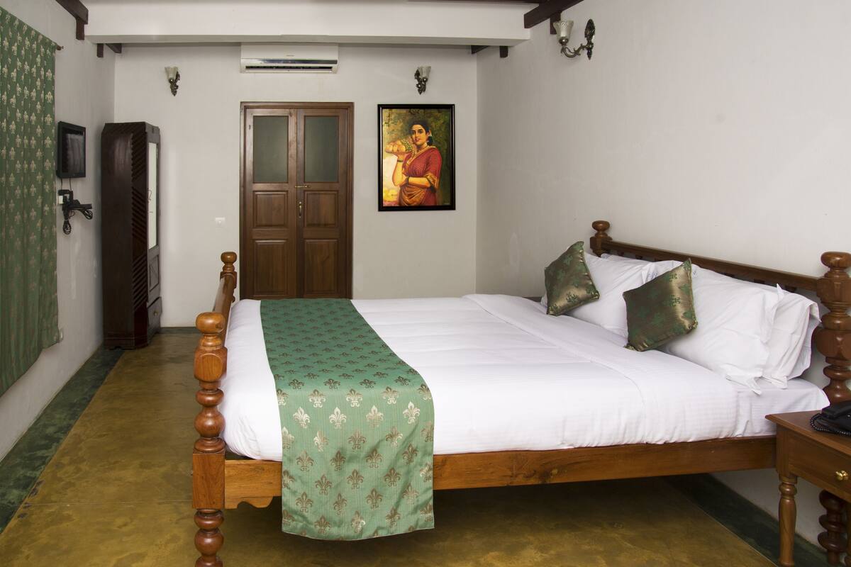 A neatly made bed with a green bedspread, a wooden headboard, and two decorative pillows.
