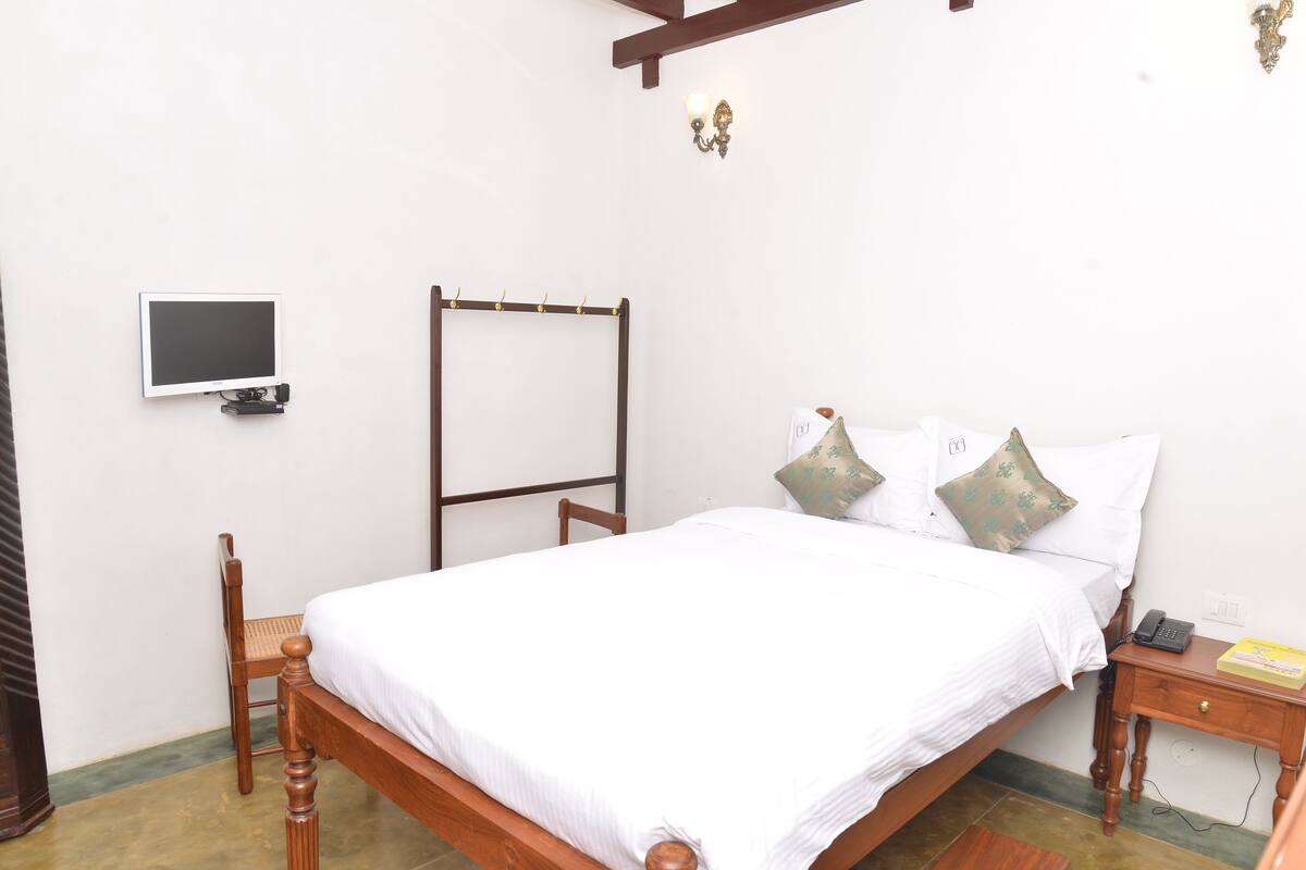 A bedroom with a wooden bed, a bedside table with a lamp, a chair, a wall-mounted TV, and a calendar.