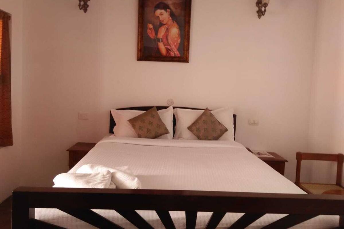 A bedroom with a bed, pillows, a nightstand, a chair, and a wall-mounted painting.