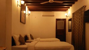Une chambre avec deux lits, un ventilateur de plafond, des appliques murales, une porte et un miroir.