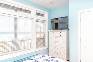Een slaapkamer met een bed, een dressoir, een televisie bovenop het dressoir en een raam met jaloezieën.
