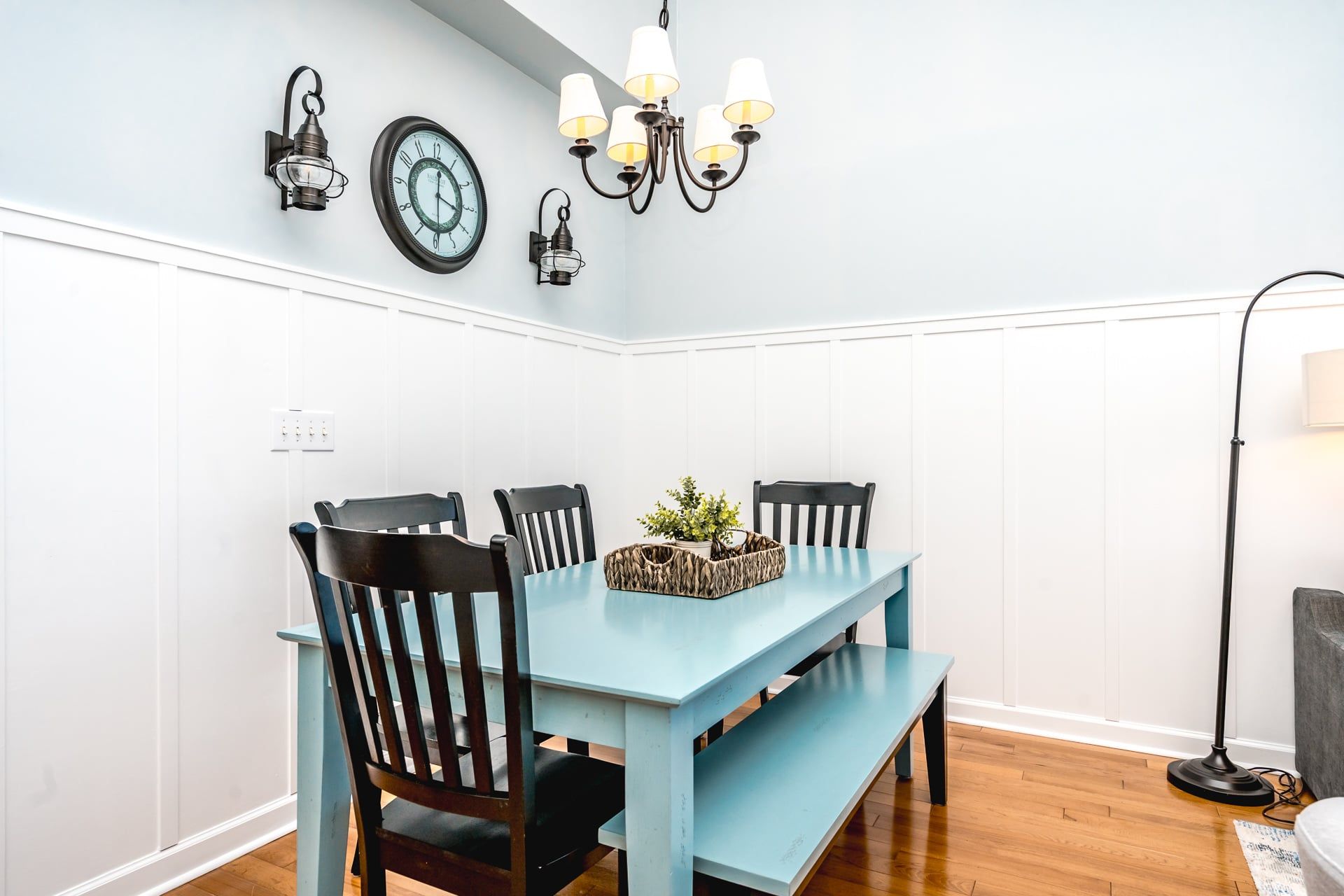 A dining area with a light blue table, black chairs, a chandelier, and wall-mounted clocks.