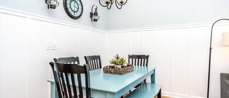 A dining area with a light blue table, black chairs, a chandelier, and wall-mounted clocks.