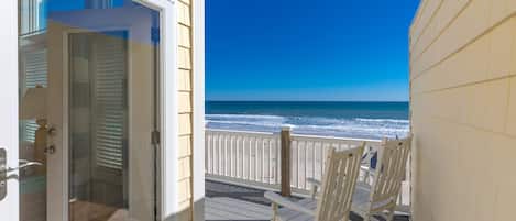 A wooden deck with white rocking chairs overlooking a beach.