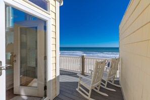 Een houten terras met witte schommelstoelen met uitzicht op een strand.
