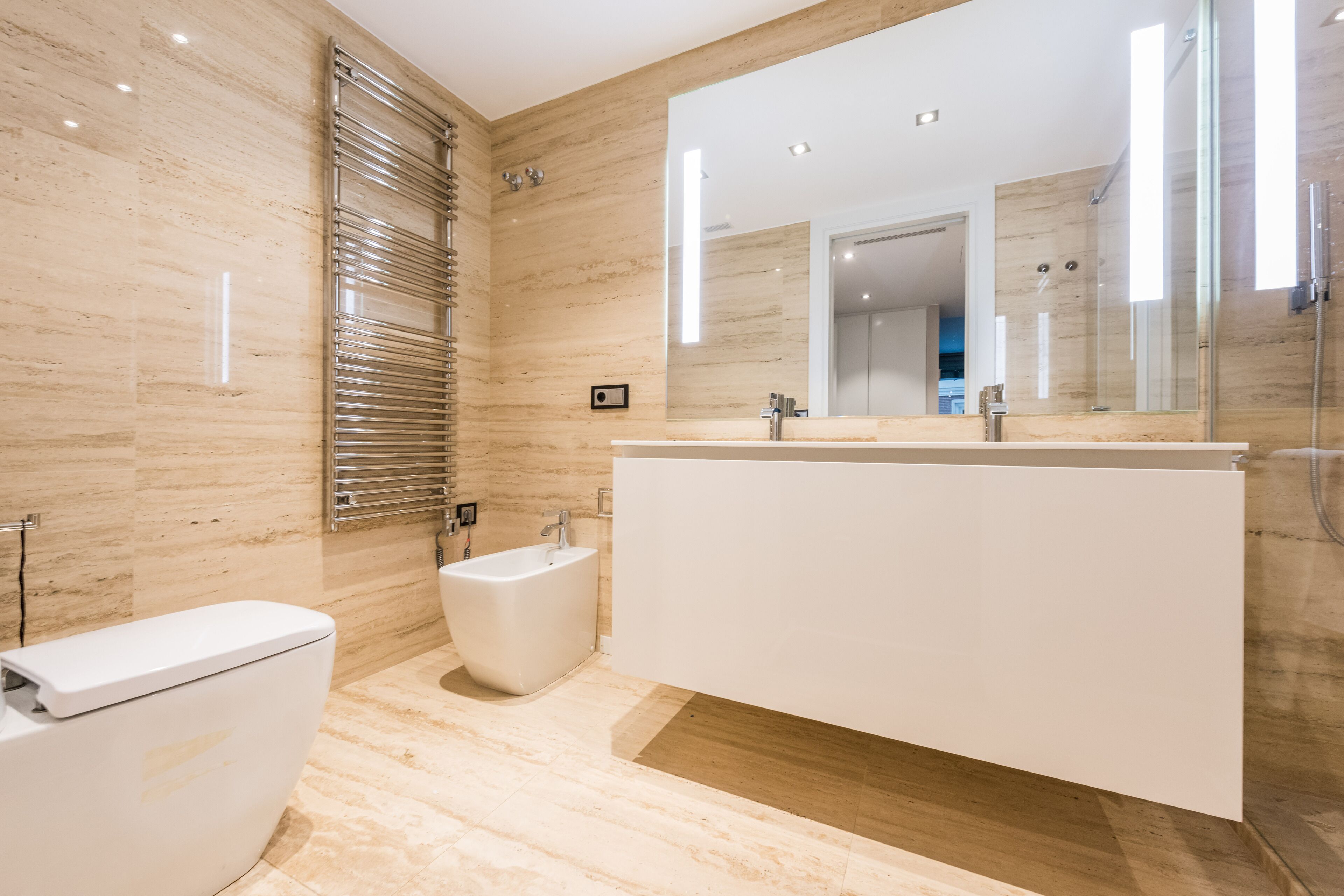 Ein modernes Badezimmer mit einem großen Spiegel, einem Bidet und einer Toilette.