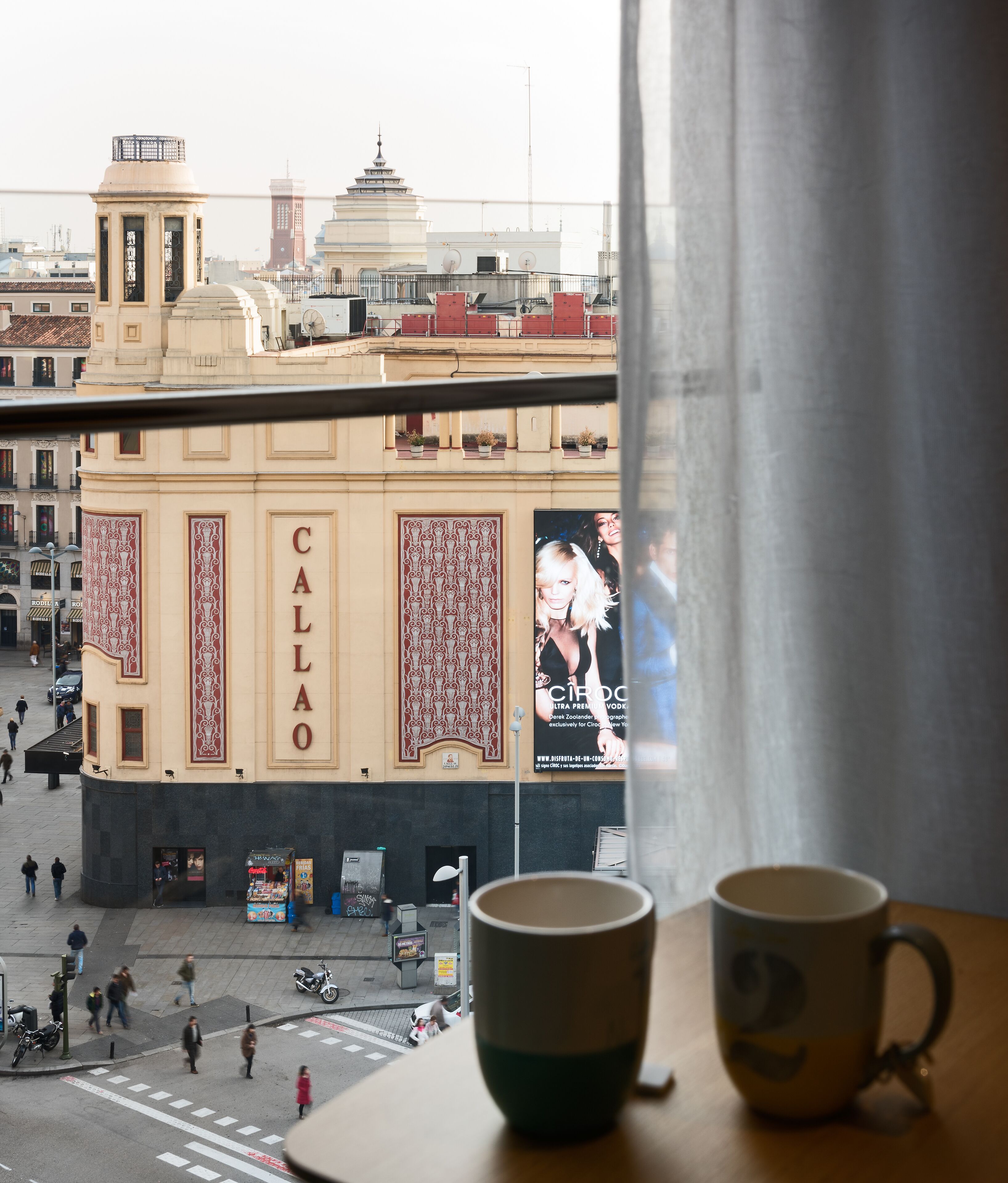 A view of a building with a large advertisement for 'Callao' and a street scene with pedestrians and parked motorcycles.