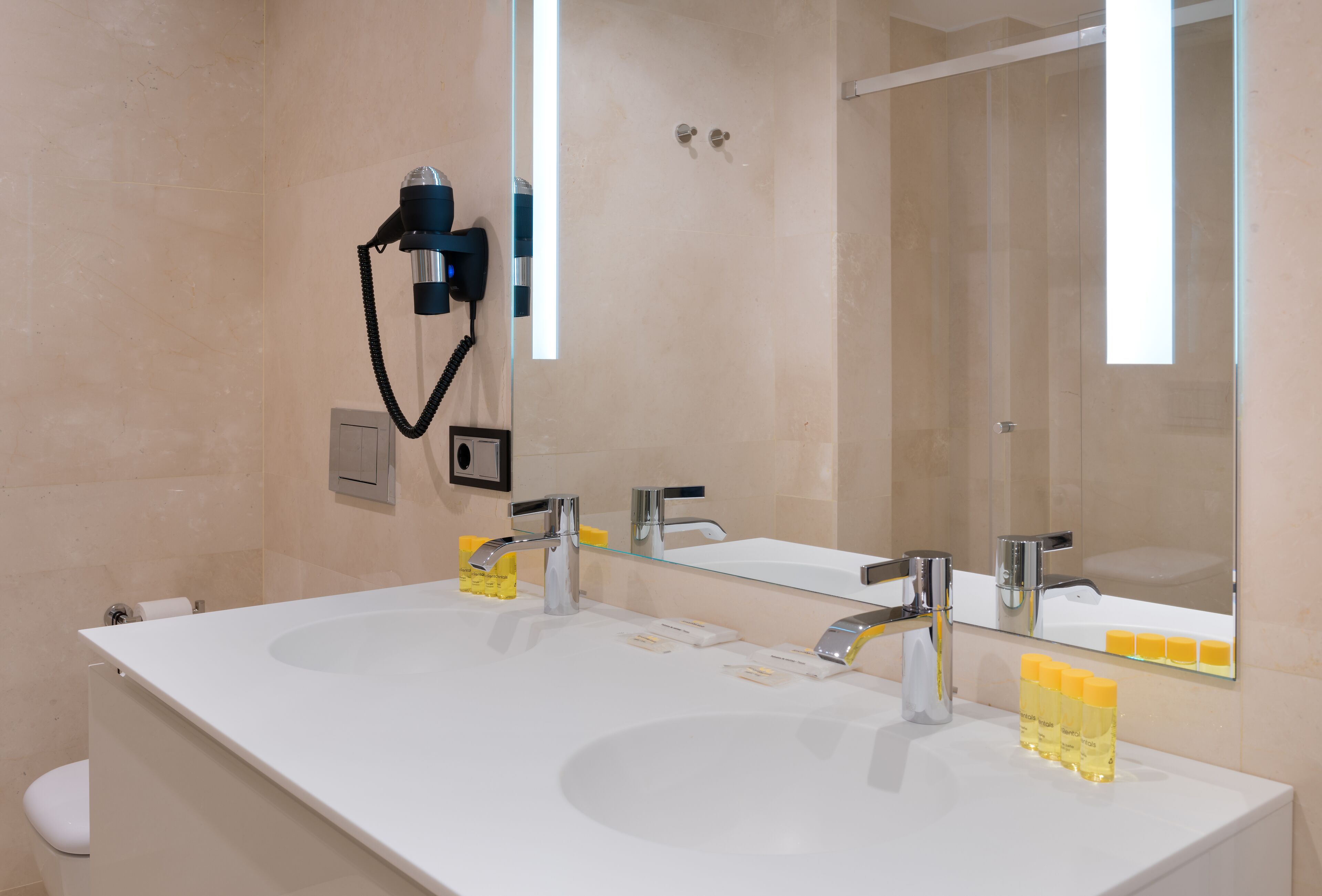 A modern bathroom with two sinks, a large mirror, and a hairdryer on the wall.