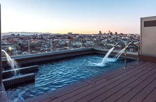Una piscina en la azotea con dos chorros de agua, rodeada de vistas a la ciudad al atardecer.