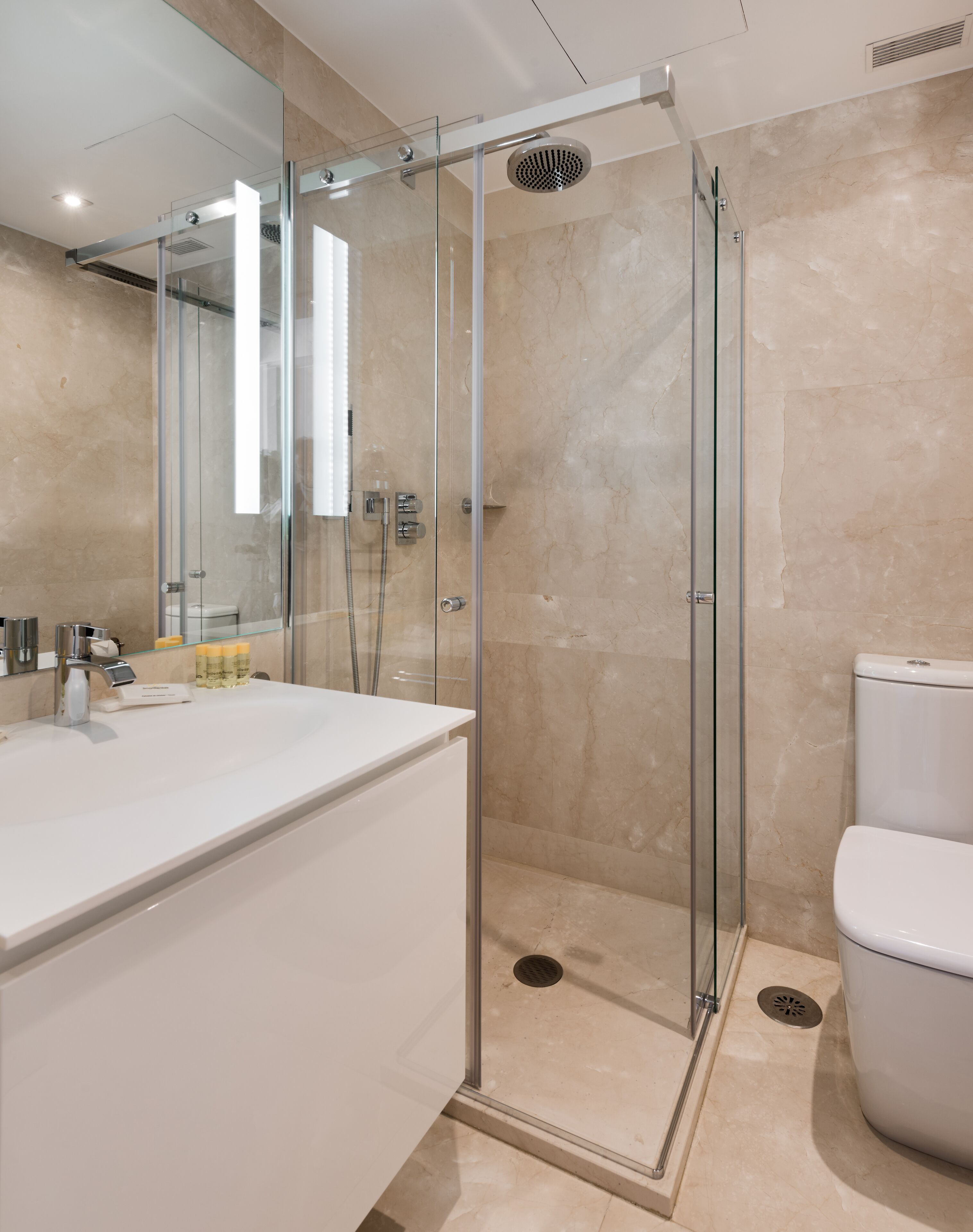 Un baño moderno con ducha de vidrio, un lavamanos blanco y un inodoro.