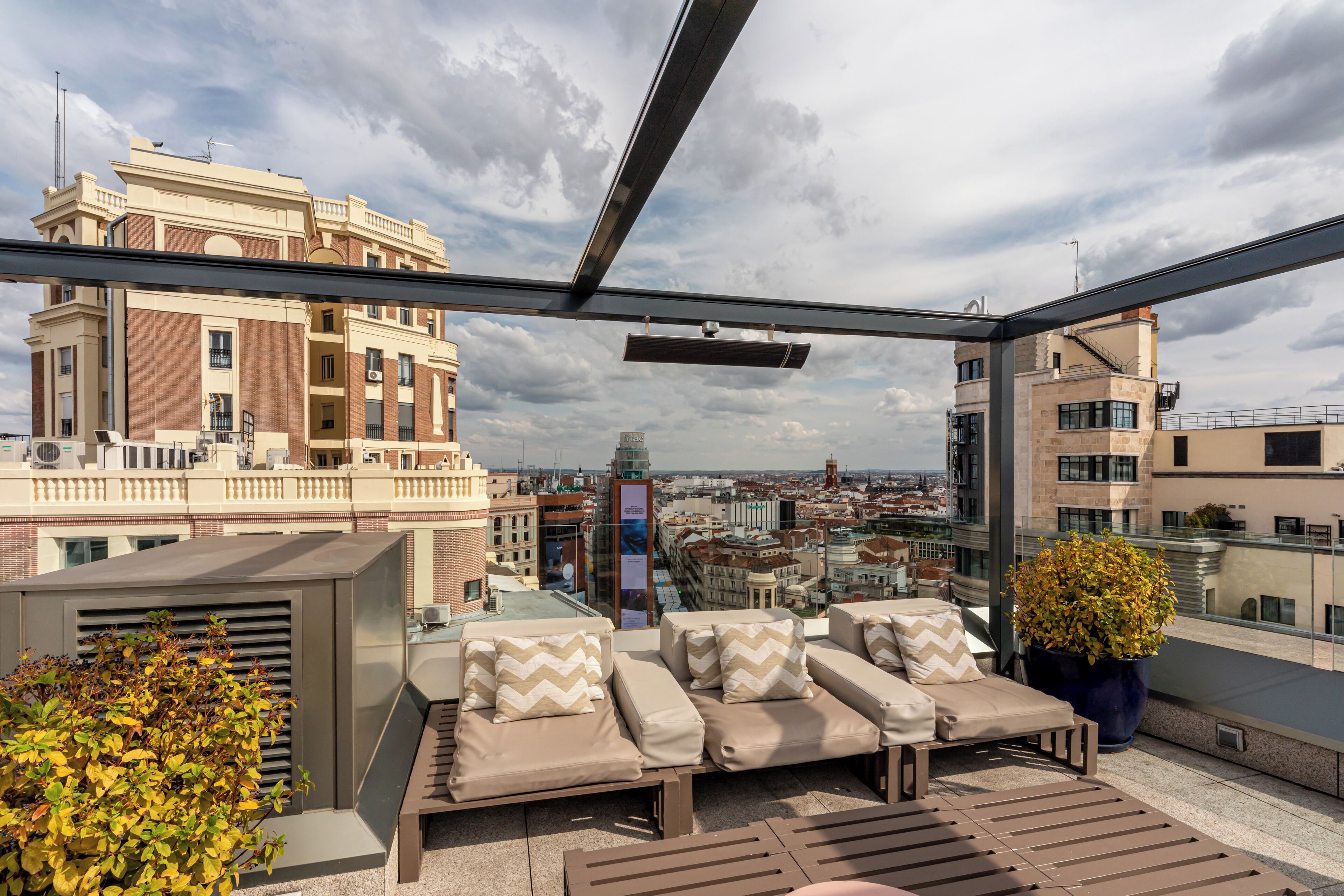 A rooftop terrace with outdoor seating, a large potted plant, and a city view.