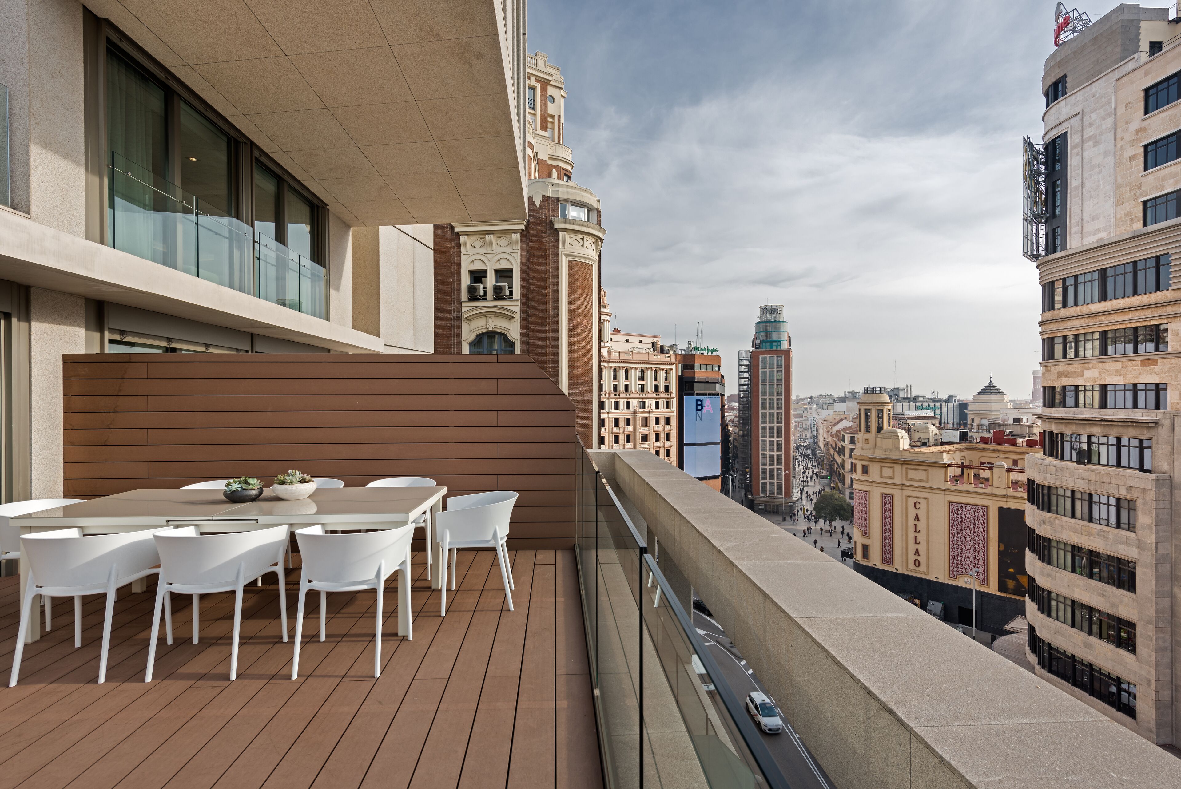 A balcony with a wooden floor, white chairs, and a table with a bowl of plants.