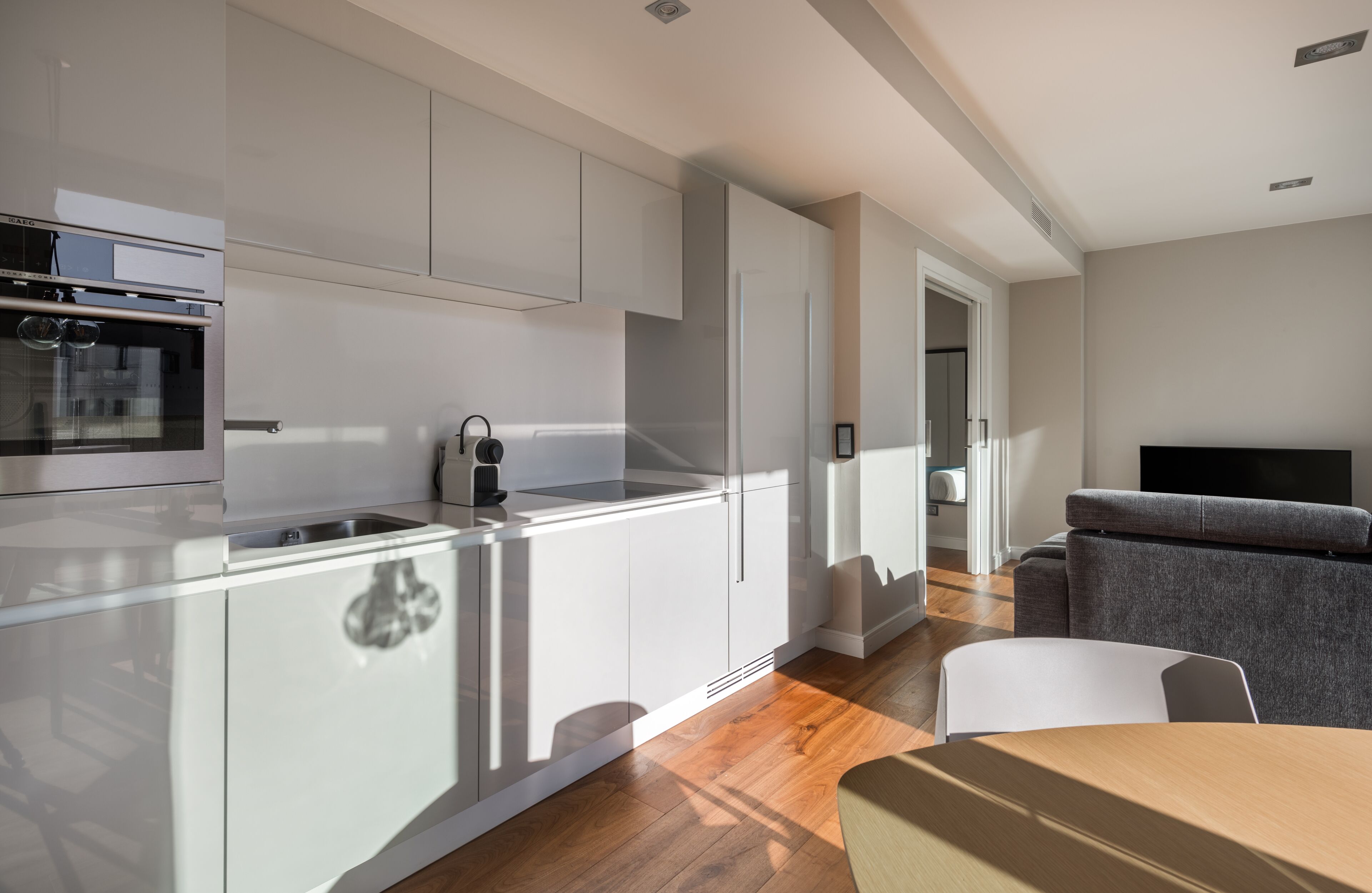 Een moderne keuken met witte kasten, een ingebouwde oven en een eethoek met een tafel en stoelen.