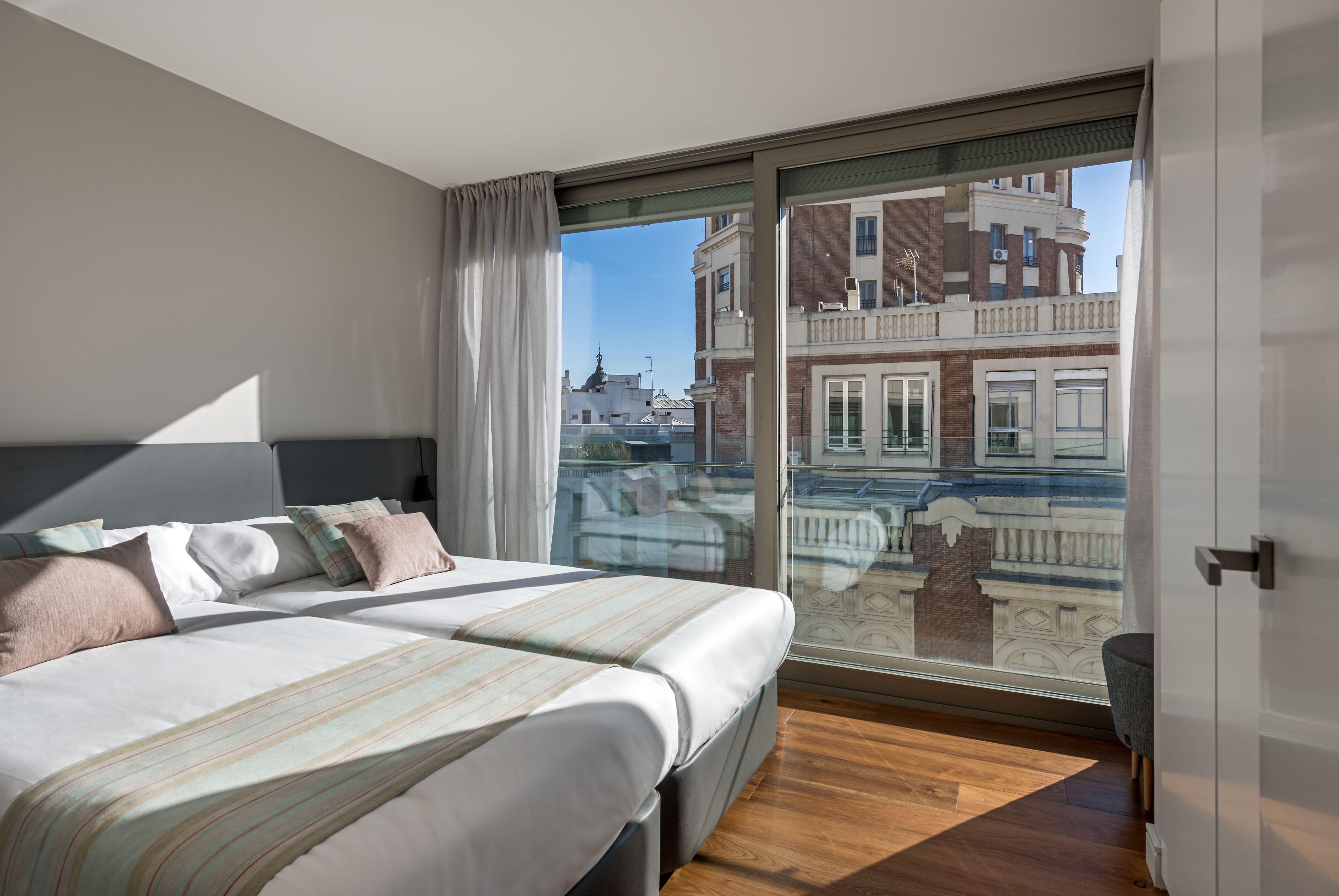 A modern hotel room with a large bed, a balcony with a city view, and a sliding glass door.