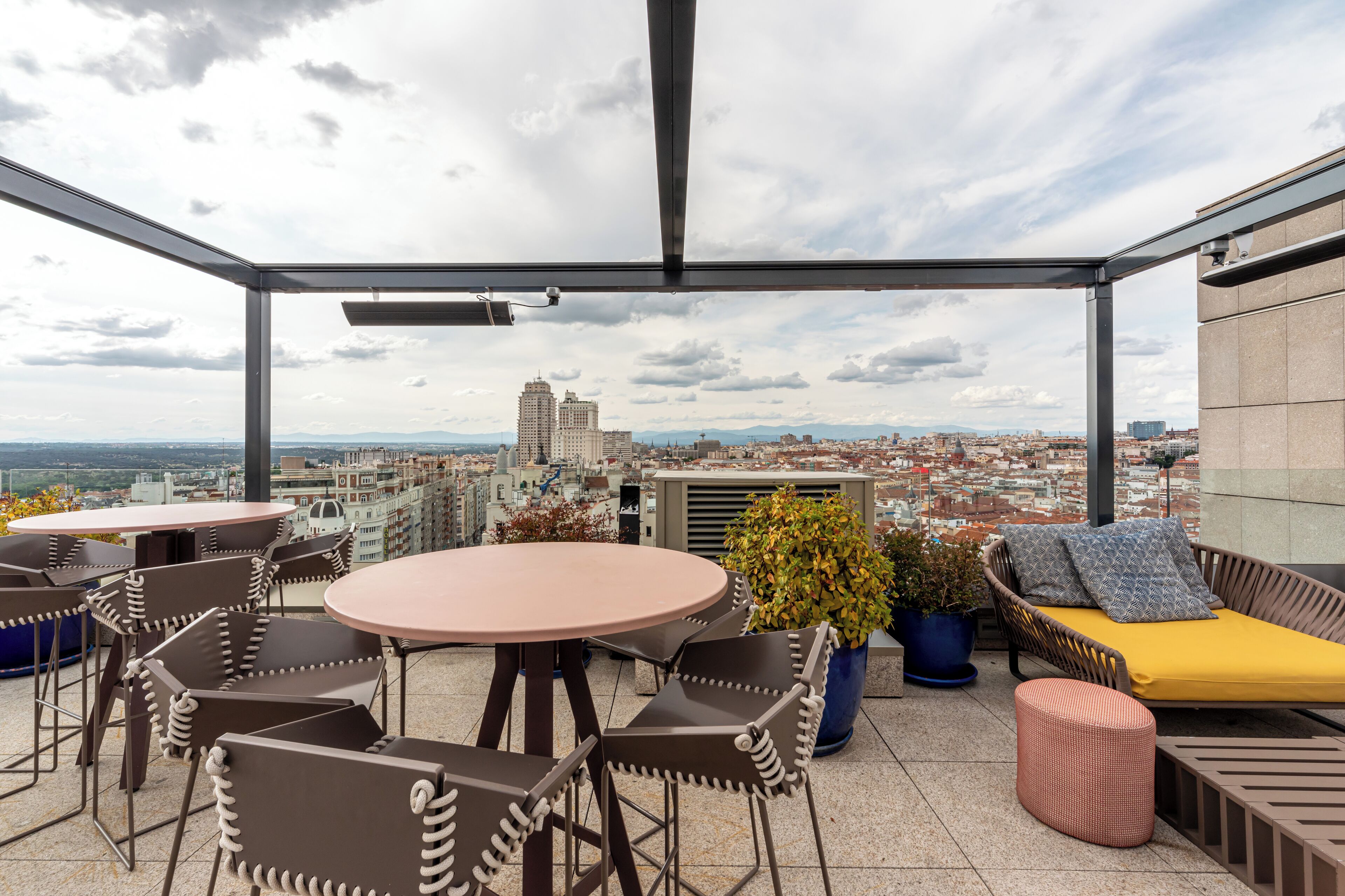 A rooftop terrace with a city view, furnished with tables, chairs, and a sofa.