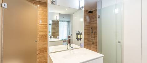 A modern bathroom with a large mirror, a white sink, and a glass shower enclosure.