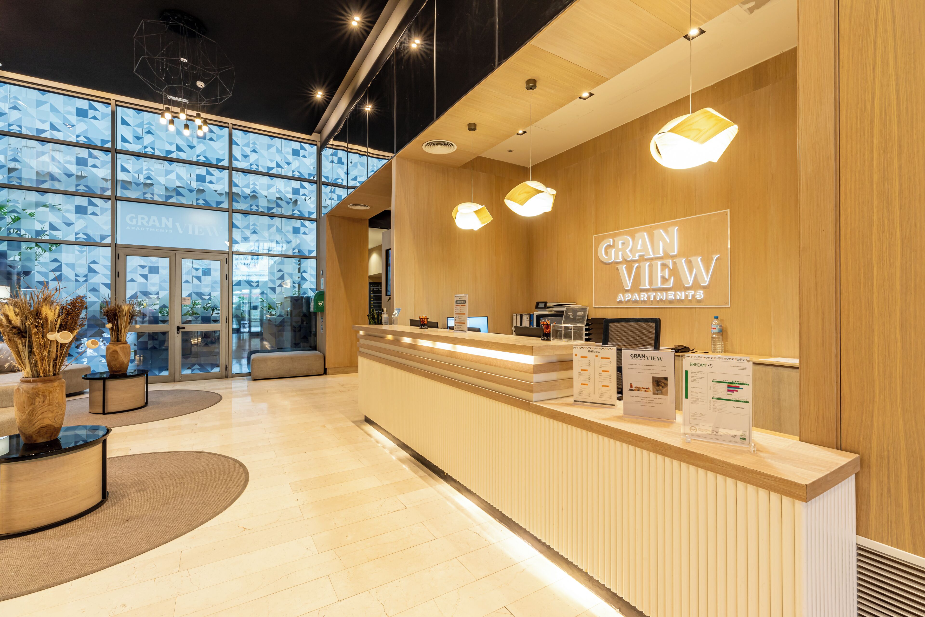 A reception area with a wooden reception desk, a large window with geometric patterns, and hanging pendant lights.