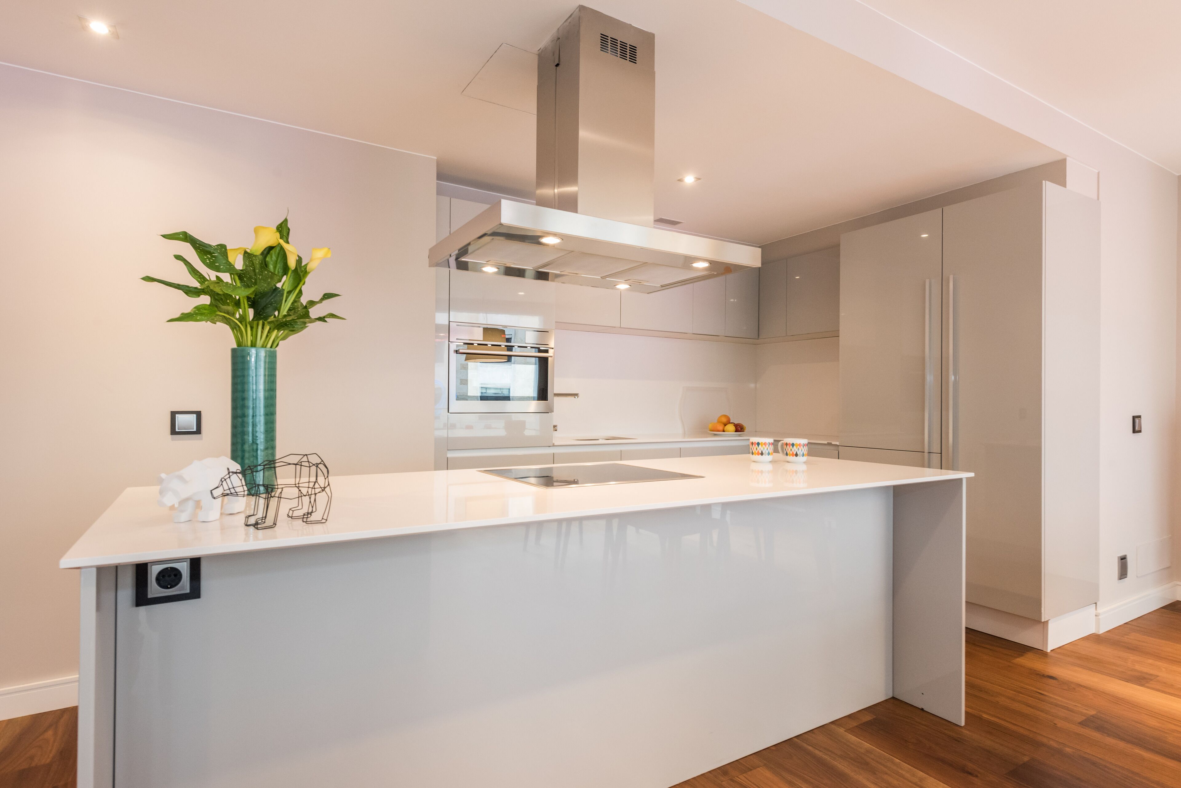 A modern kitchen with a white island, stainless steel appliances, and a green vase with flowers.