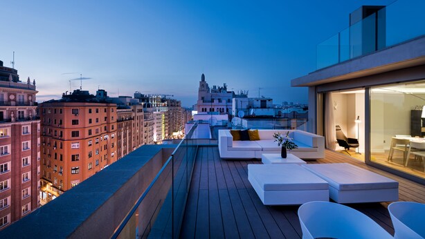 A rooftop terrace with modern outdoor seating, a view of the cityscape, and a building with a tower in the background. - Gran View Apartments (Madrid)