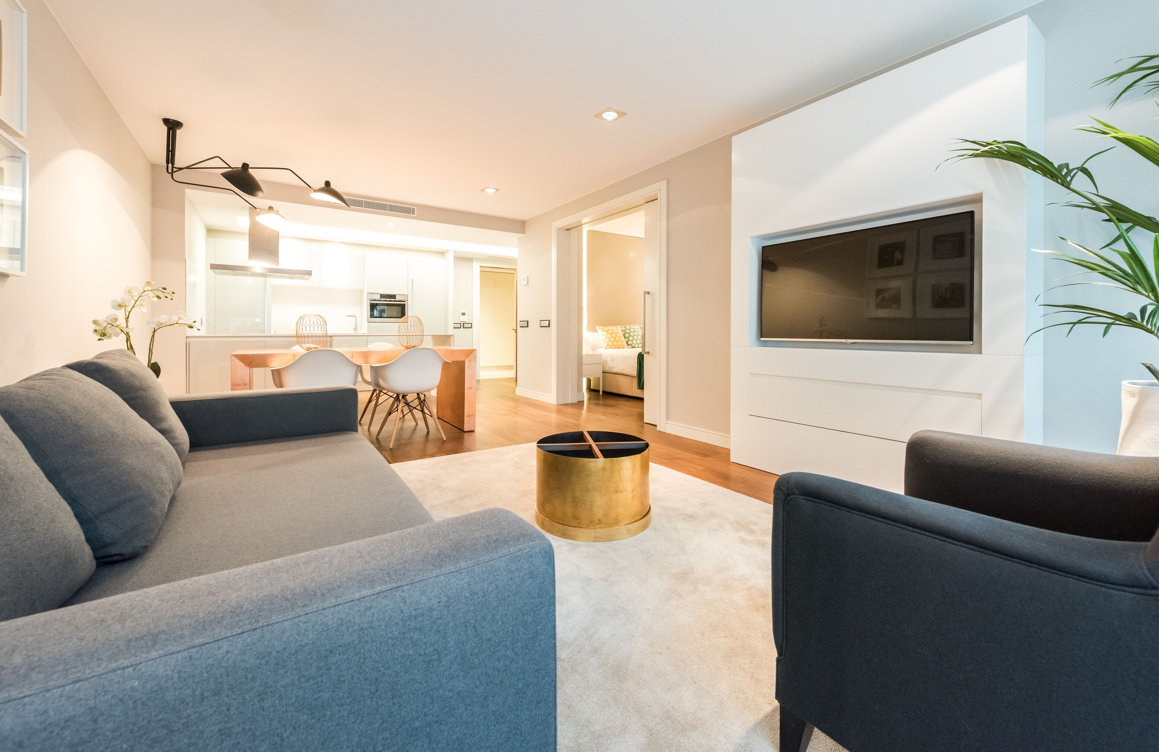 A modern living room with a sofa, armchair, and a TV mounted on the wall.