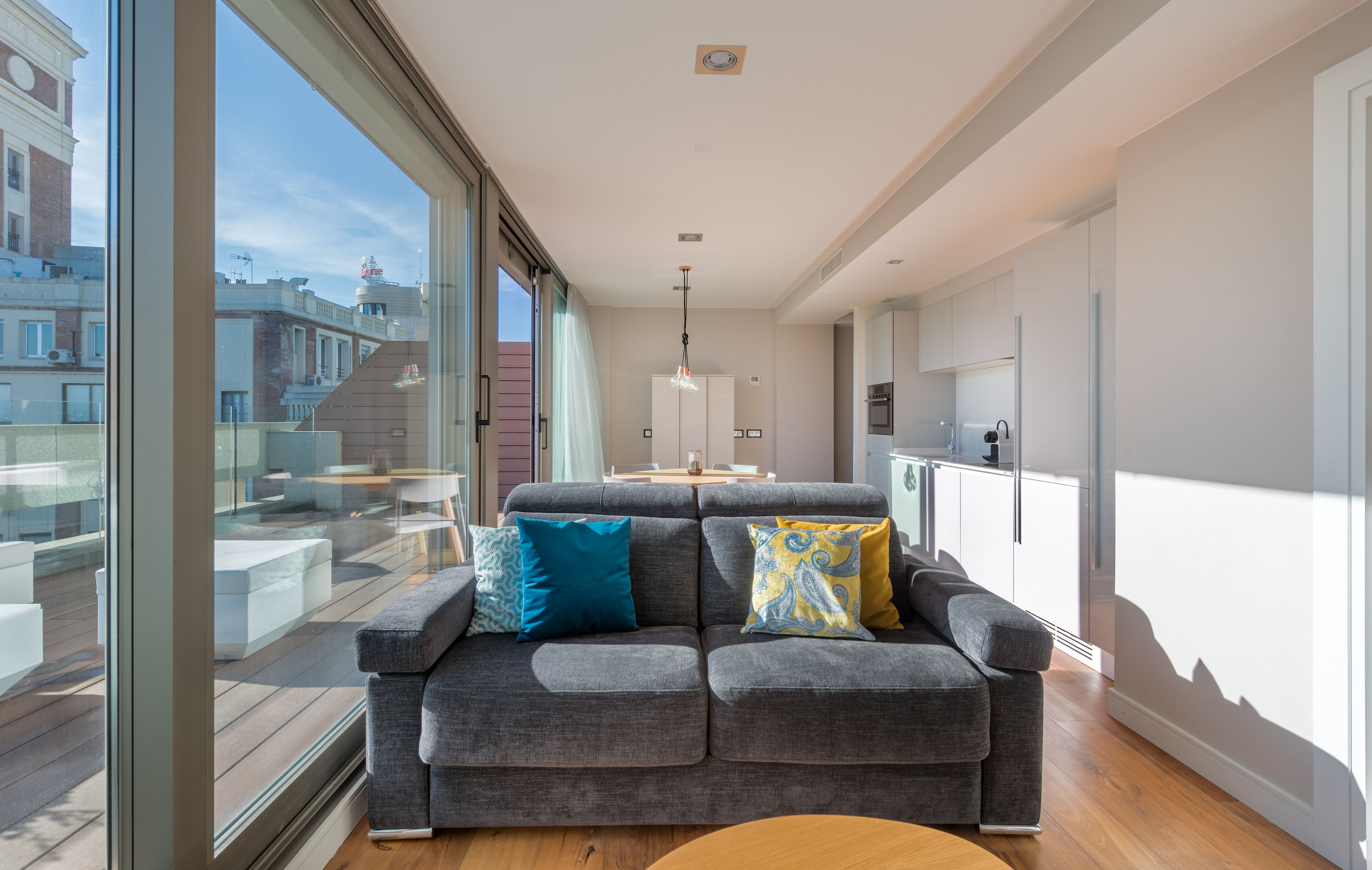 Ein modernes Wohnzimmer mit grauem Sofa, einem Holztisch und einem großen Fenster mit Blick auf die Stadt.