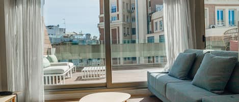 A balcony with a sofa and two tables, overlooking a cityscape with buildings and boats.